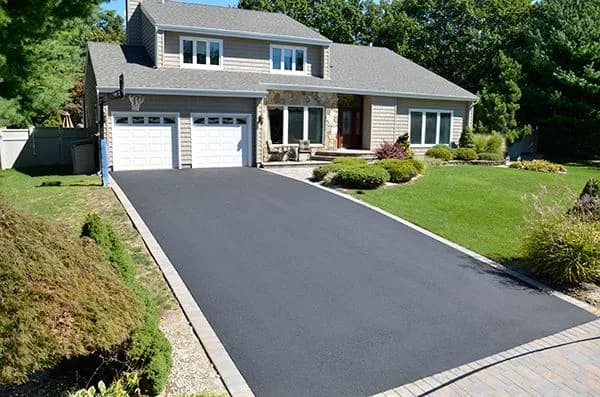 Wide newly paved residential asphalt driveway with Belgian block edging in front of two-car garage home in Edison, NJ