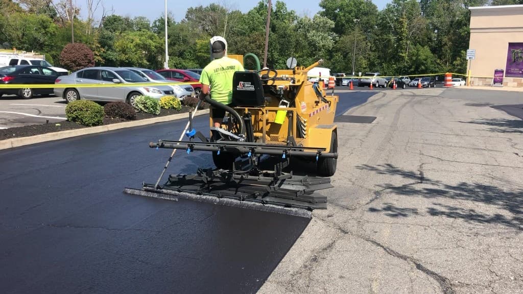 A-1 Asphalt Paving crew member applying fresh seal-coat with professional squeegee machine on commercial parking lot in Metuchen, NJ